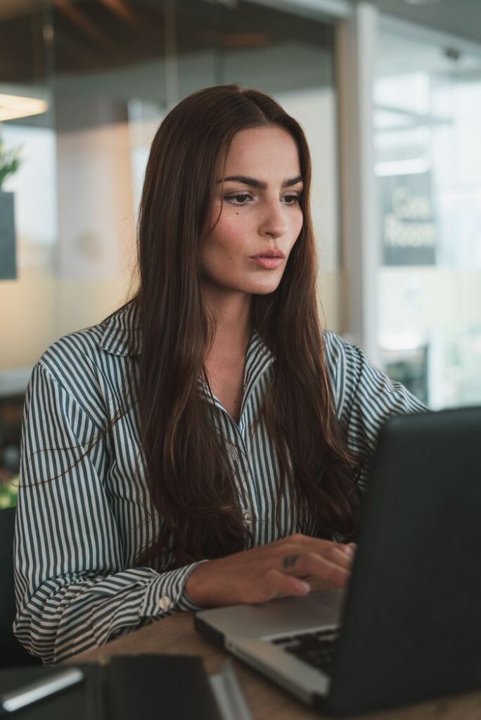 Focused businesswoman with long hair working on a laptop in a modern office environment.